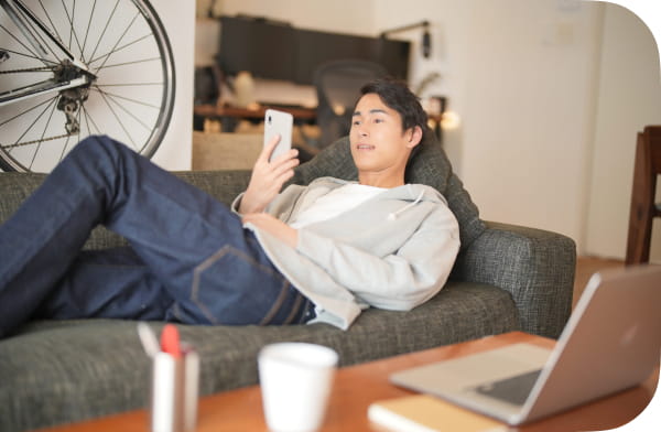 男性がソファでくつろぎながらスマホを見ている様子